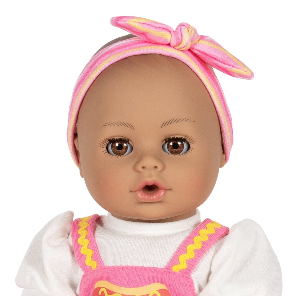 Adora Hot Diggity Dog baby doll set includes one 13-inch doll, a hot dog-printed one-piece dress with white undershirt, matching headband, white bloomers, and a pink baby bottle. Made for Ages 1+.