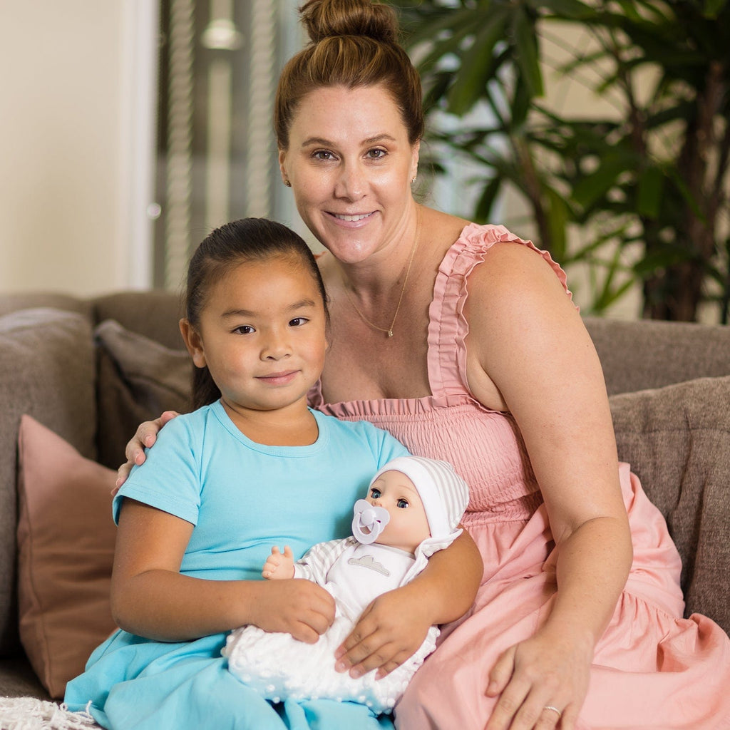 Gender-neutral baby doll set comes with one 16" weighted baby doll, a Certificate of Adoption, a pacifier, a hospital bracelet, a disposable diaper, a baby blanket, a crib, and a removable striped, cloud-print onesie with a matching cap.